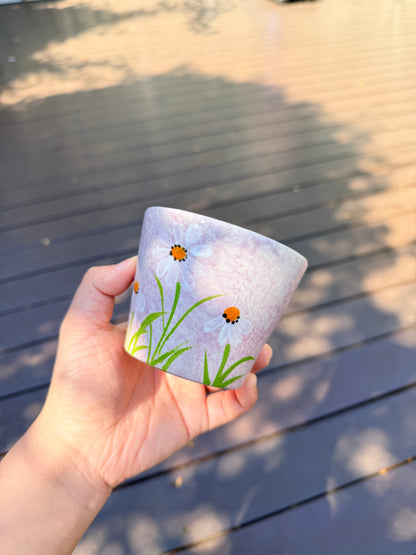 Hand holding a 270ml pink ceramic cup with hand-painted white daisies and green leaves
