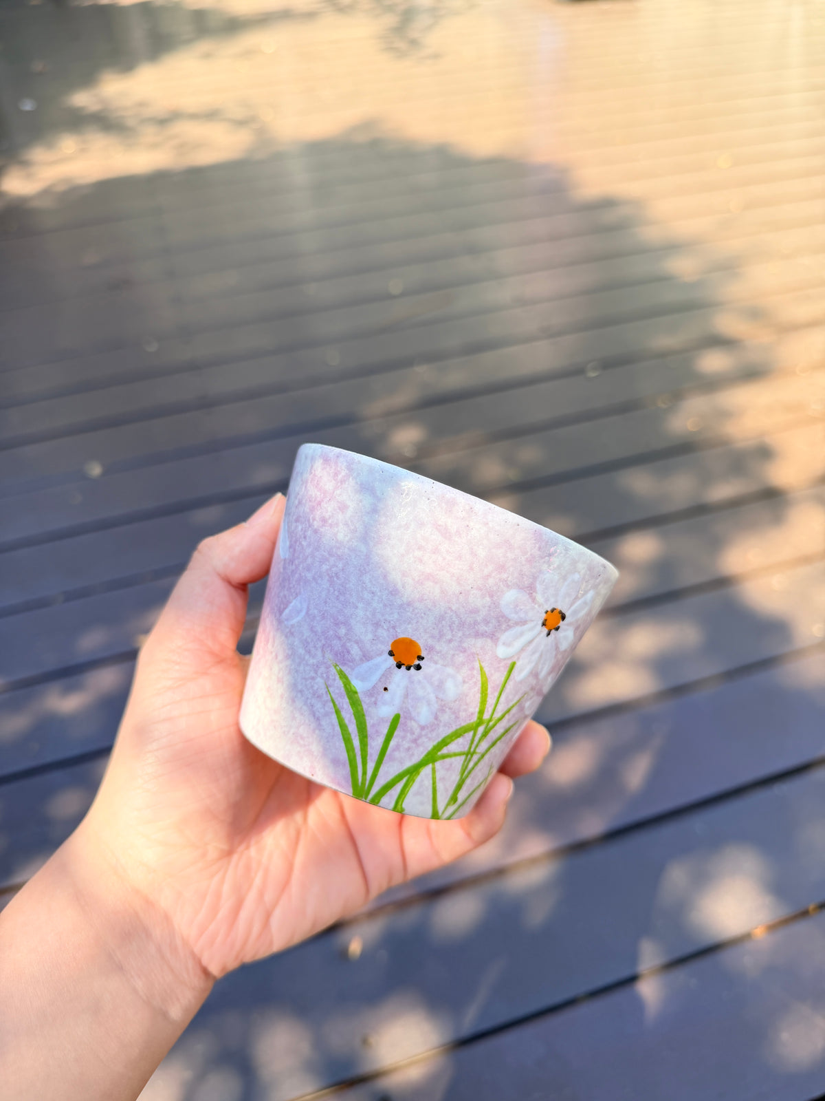 Hand holding a 270ml pink ceramic cup with hand-painted white daisies and green leaves