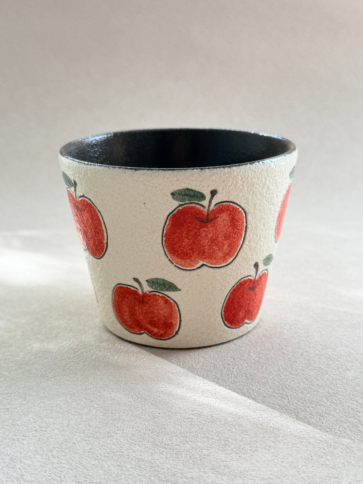 Front view of a red apple ceramic cup with a textured ivory finish and dark glazed interior.