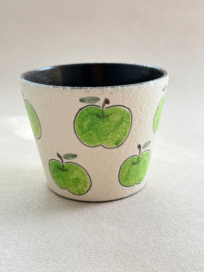 Front view of a green apple ceramic cup with a textured ivory finish and dark glazed interior.