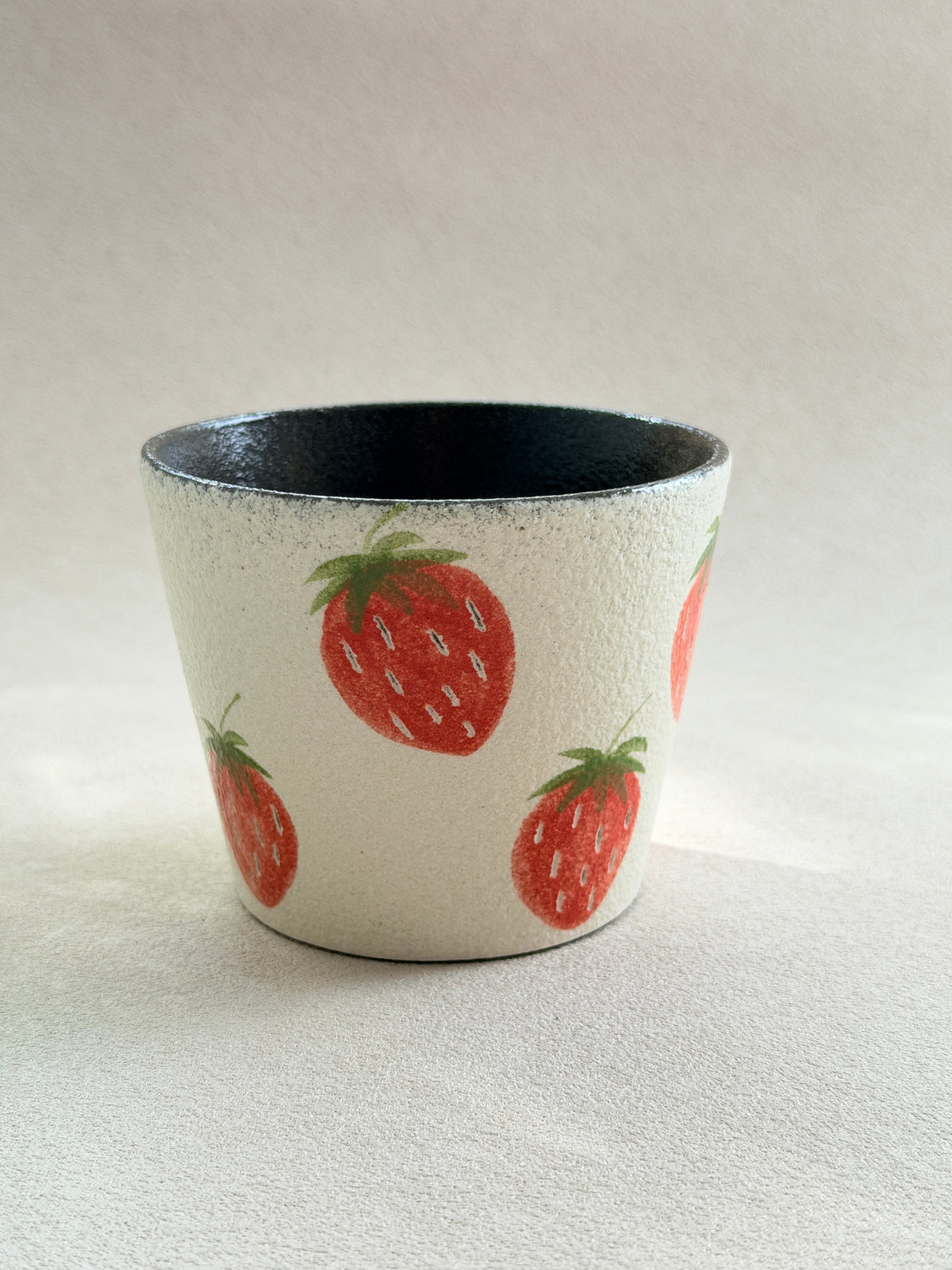 Front view of a hand-painted strawberry pottery clay cup with a textured ivory exterior and dark glazed interior.
