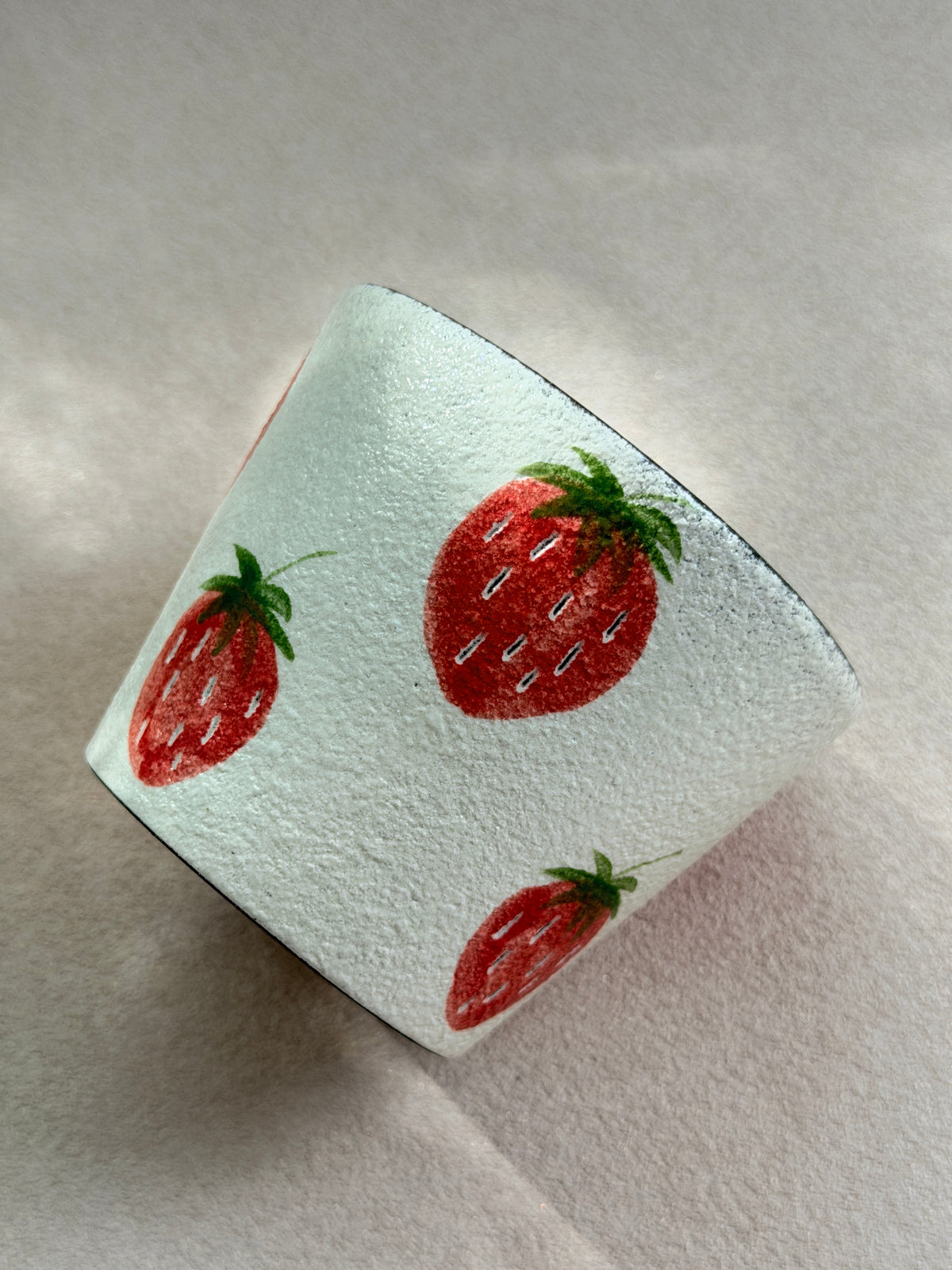Side view of the strawberry pottery clay cup showing its textured ivory surface and hand-painted fruit design.
