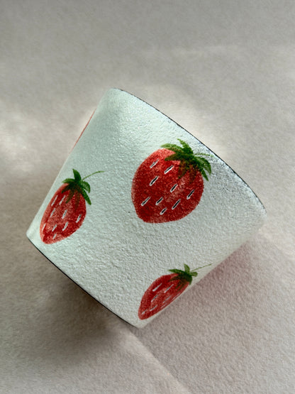 Side view of the strawberry pottery clay cup showing its textured ivory surface and hand-painted fruit design.
