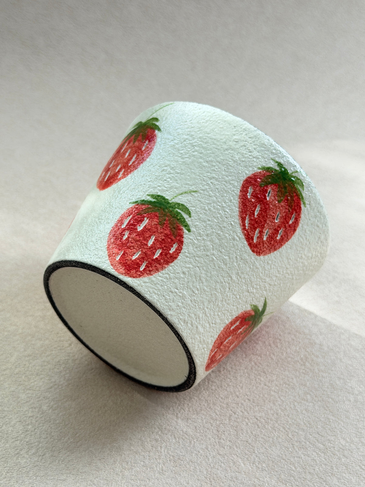 Angled view of the hand-painted strawberry cup showing the wraparound design and ceramic base.

