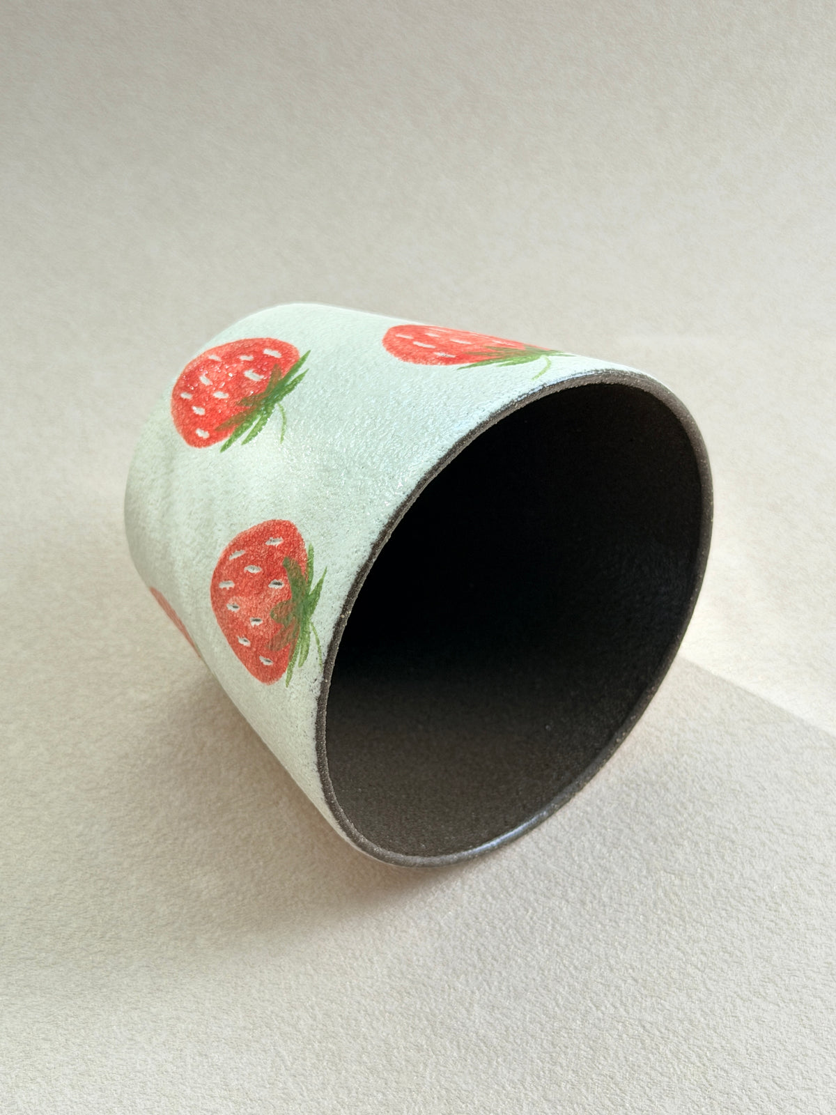 Strawberry pottery clay cup resting on its side, showing the dark glazed interior and textured exterior.
