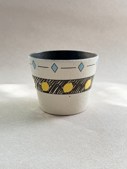 Front view of a hand-painted lemon pottery clay cup with a textured ivory finish, blue geometric details and dark glazed interior.
