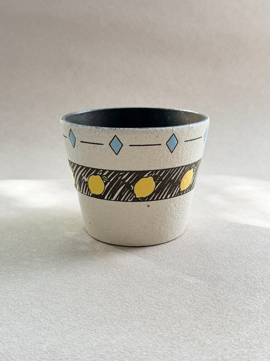 Front view of a hand-painted lemon pottery clay cup with a textured ivory finish, blue geometric details and dark glazed interior.
