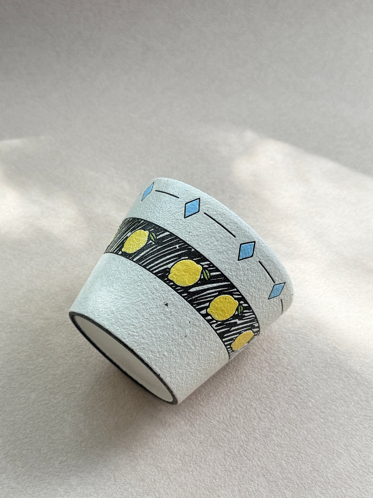 Angled side view of the lemon pottery clay cup showing its illustrated fruit band and textured surface.
