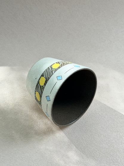 Hand-painted lemon cup resting on its side, showing the dark glazed interior and wraparound geometric design.
