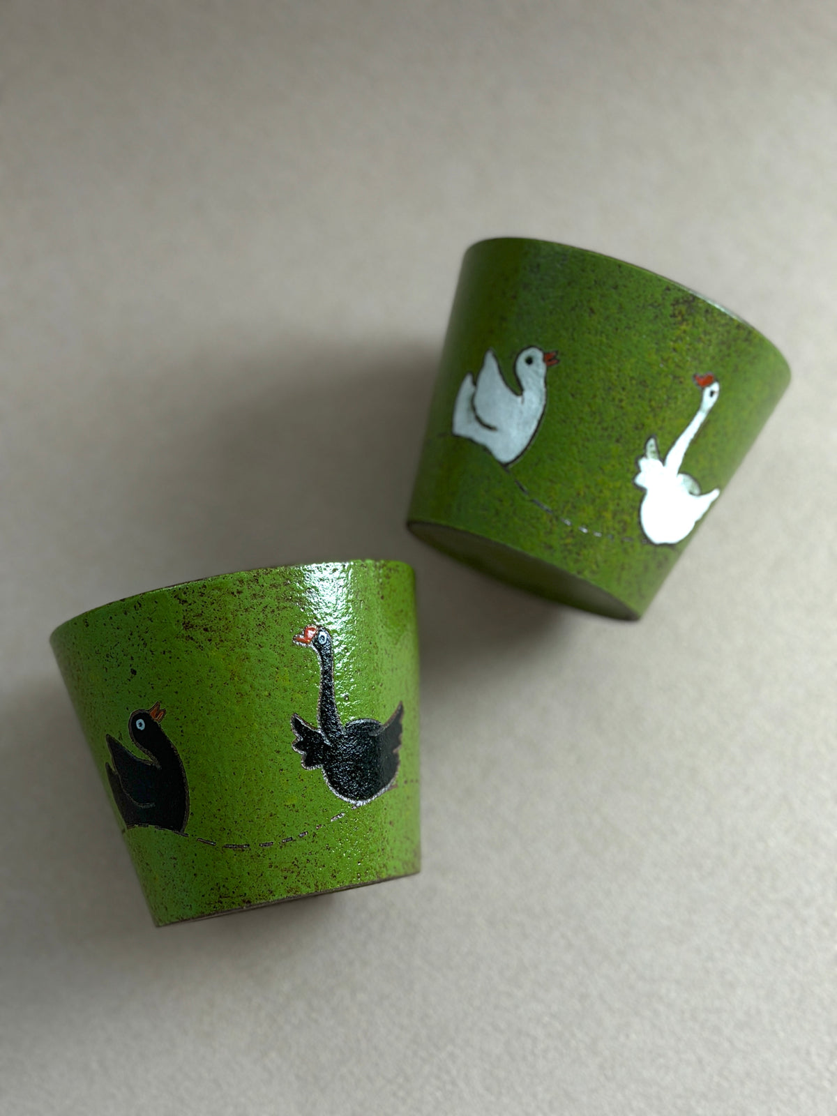 Black and white hand-painted goose ceramic cups with textured green finishes and dark glazed interiors.