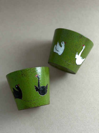 Black and white hand-painted goose ceramic cups with textured green finishes and dark glazed interiors.