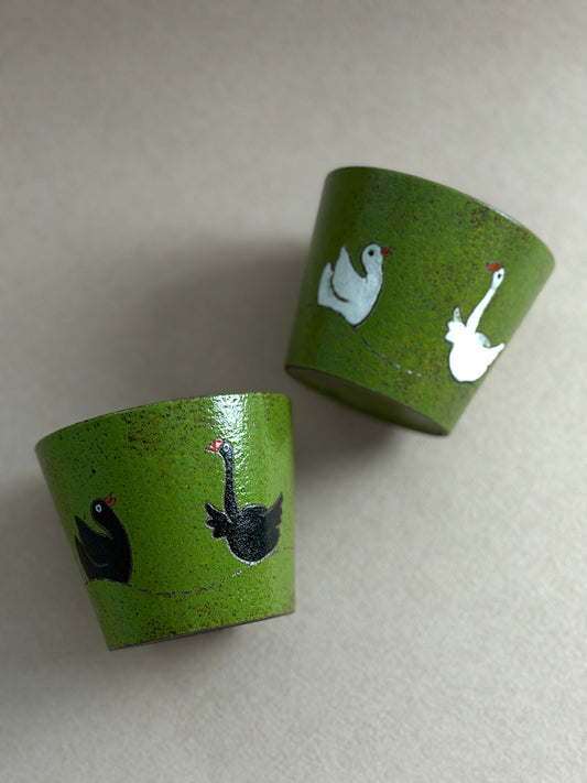 Black and white hand-painted goose ceramic cups with textured green finishes and dark glazed interiors.