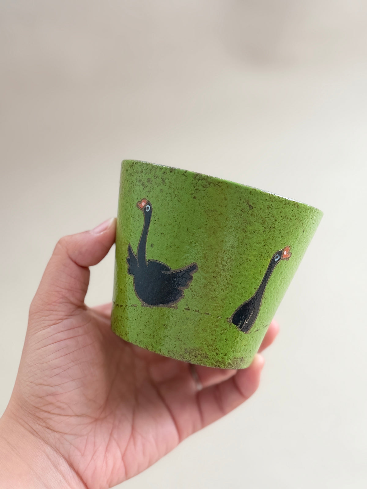 Side view of a hand-painted black goose ceramic cup held in one hand.