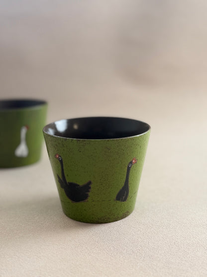 Front view of a black goose ceramic cup with a textured green finish.