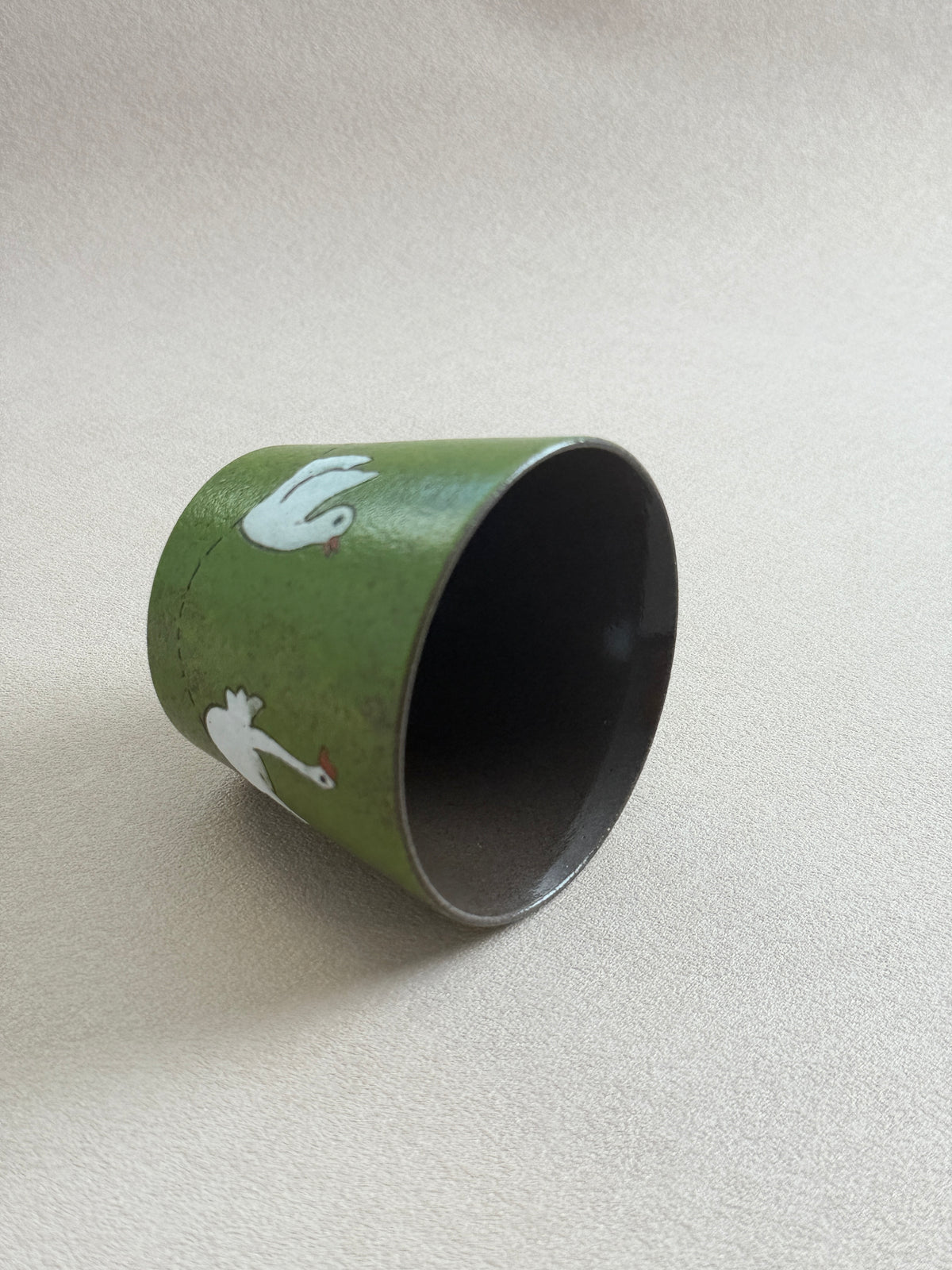 White goose ceramic cup resting on its side, showing the dark glazed interior.