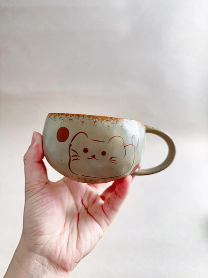 Hand holding a 270ml cream ceramic mug decorated with a hand-painted lucky cat face.