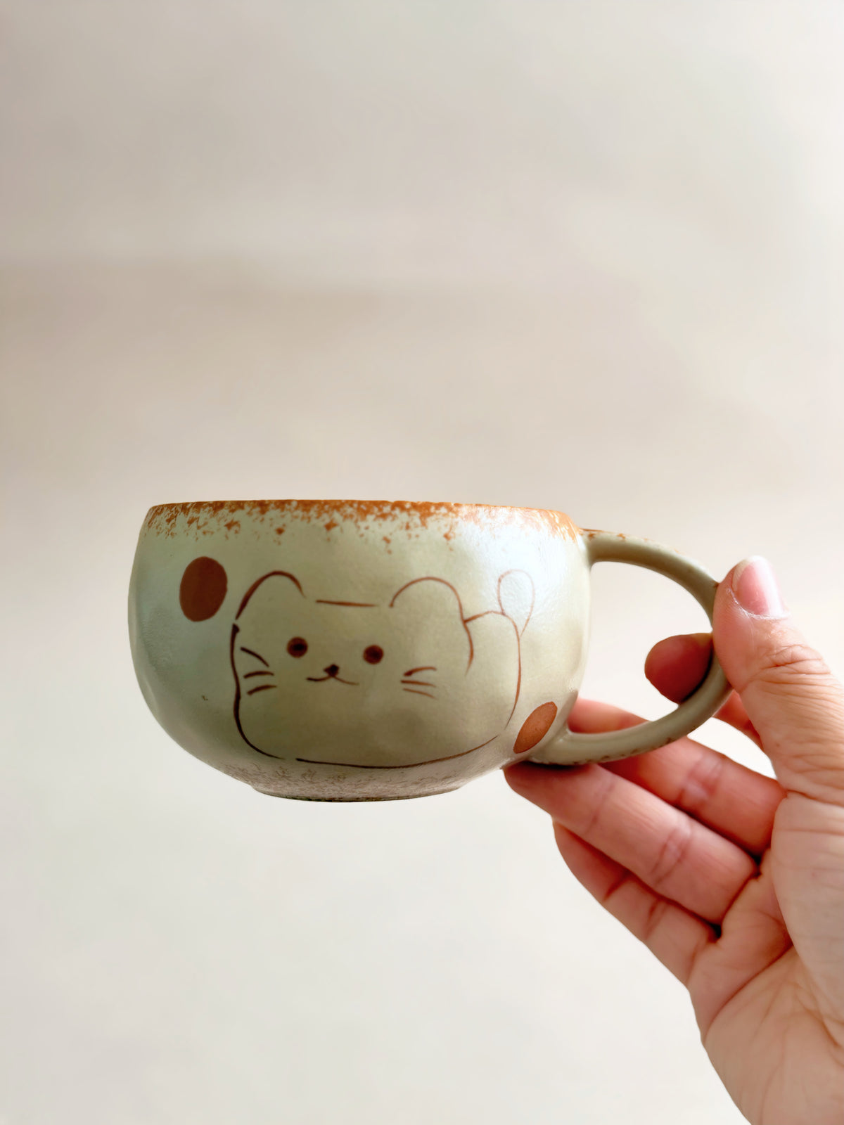 Side view of the hand-painted lucky cat ceramic mug held by its rounded handle.