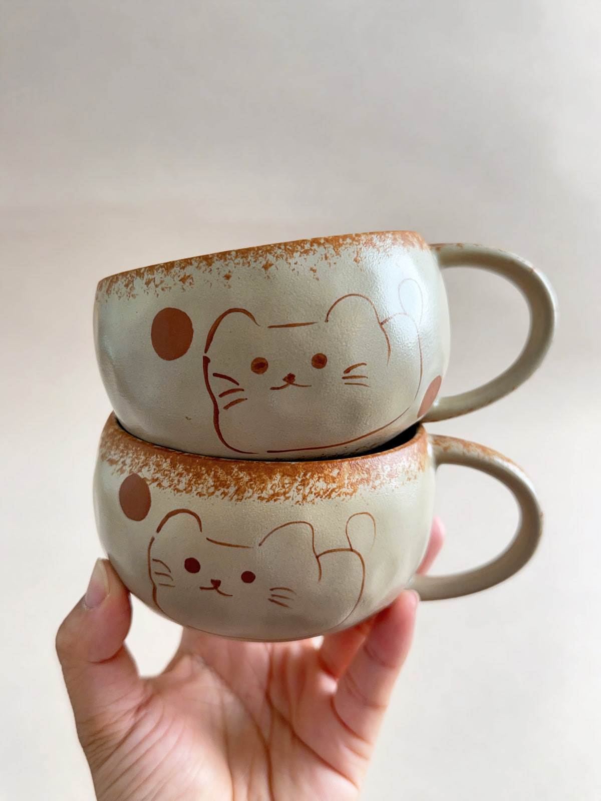 Two hand-painted lucky cat ceramic mugs stacked together on a neutral background.