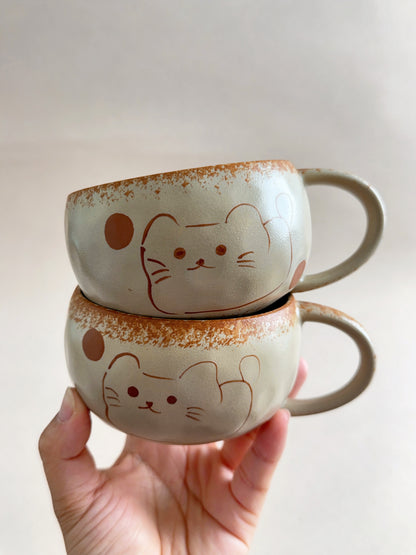 Two hand-painted lucky cat ceramic mugs stacked together on a neutral background.