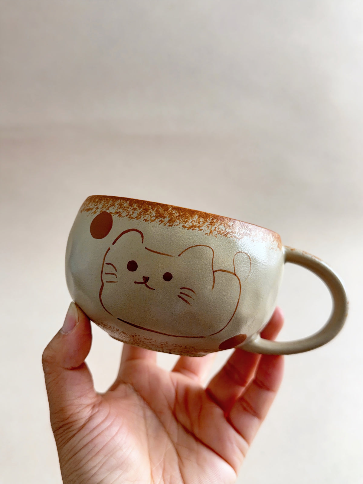 Angled view of a cream lucky cat mug showing its rounded shape and rust-red details.