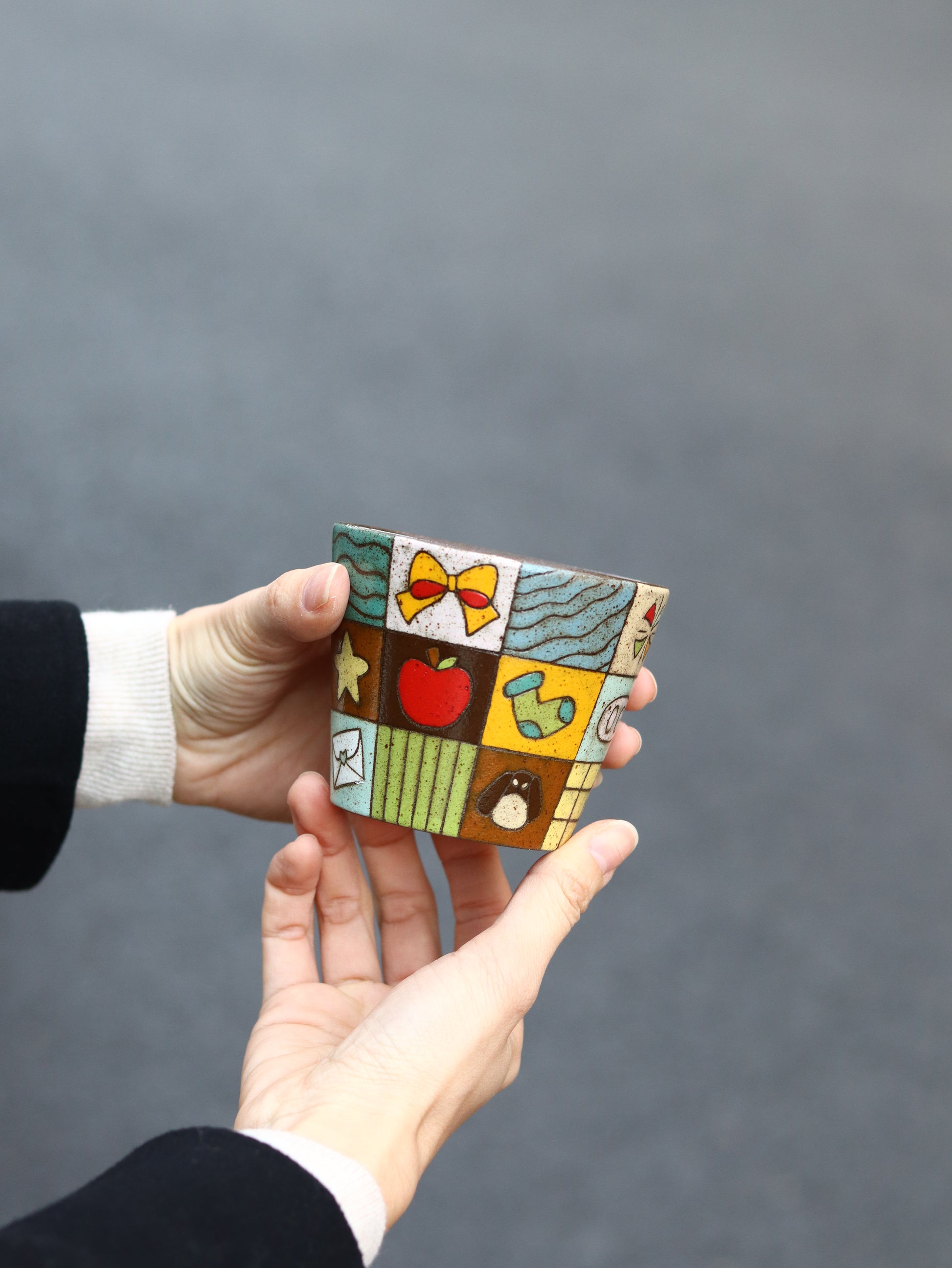 Hand holding a small, colorful ceramic piece against a gray background