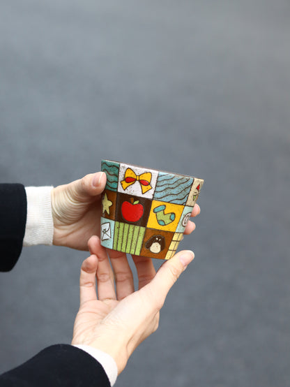 Hand holding a small, colorful ceramic piece against a gray background
