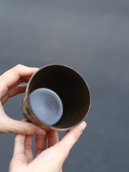 Person holding a dark ceramic cup against a gray background