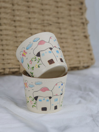 Two small containers with hand-painted designs of dogs and houses on a white surface.
