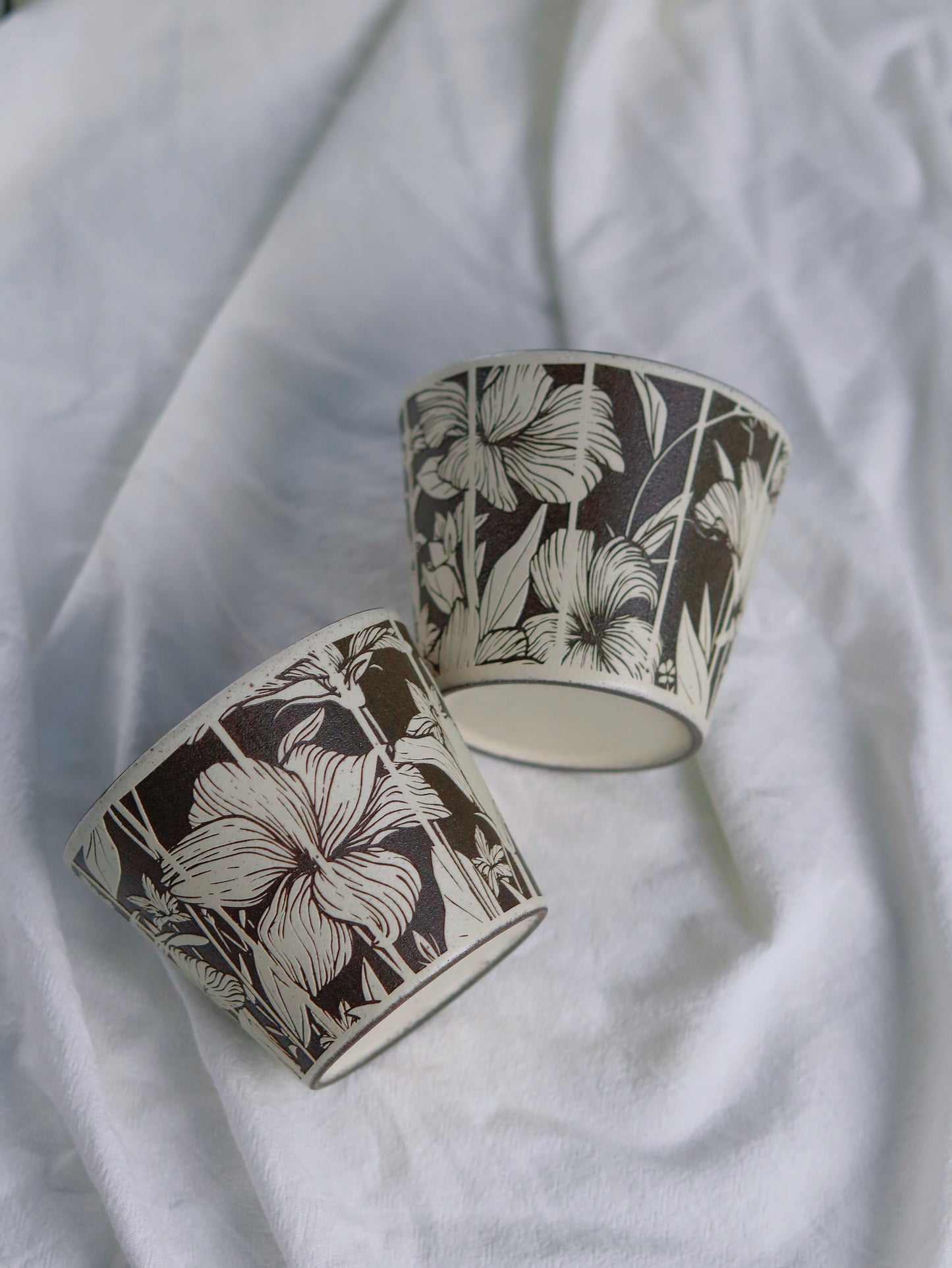 Two botanical ceramic cups showing carved floral patterns and base