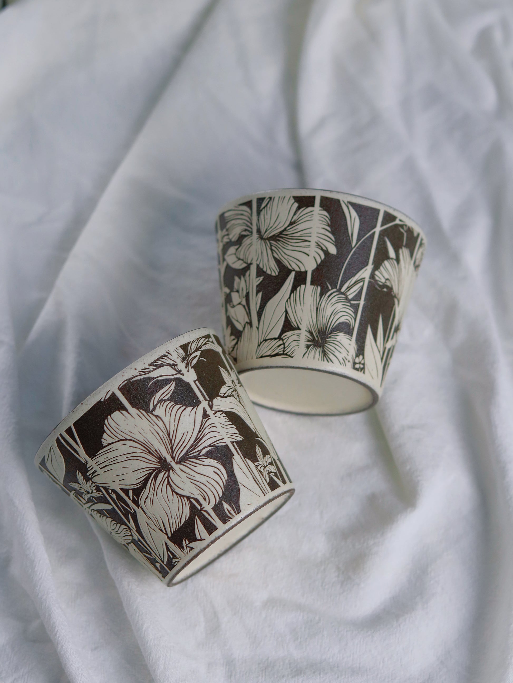 Two botanical ceramic cups showing carved floral patterns and base