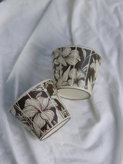 Two botanical ceramic cups showing carved floral patterns and base
