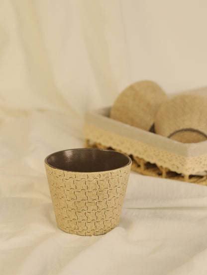 Hand-carved geometric ceramic cup with a warm beige textured finish and dark glazed interior.