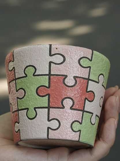 Close-up of a hand-painted puzzle ceramic cup with carved outlines in pink, green and ivory