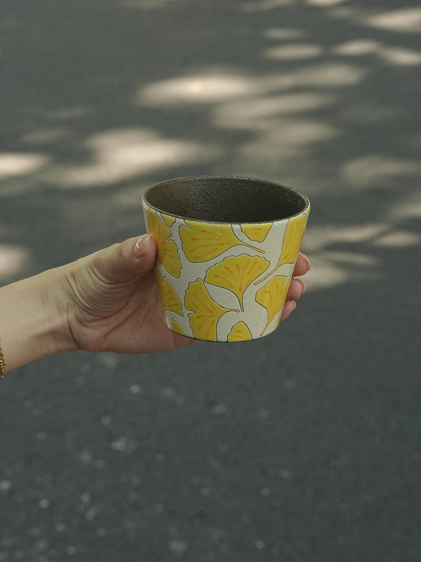 Hand holding a 270ml hand-painted ginkgo ceramic cup with carved yellow leaf outlines