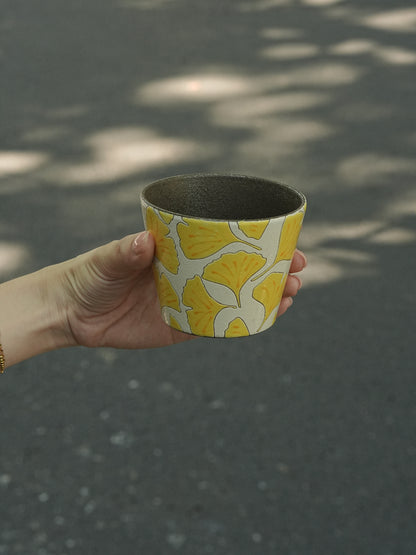 Hand holding a 270ml hand-painted ginkgo ceramic cup with carved yellow leaf outlines