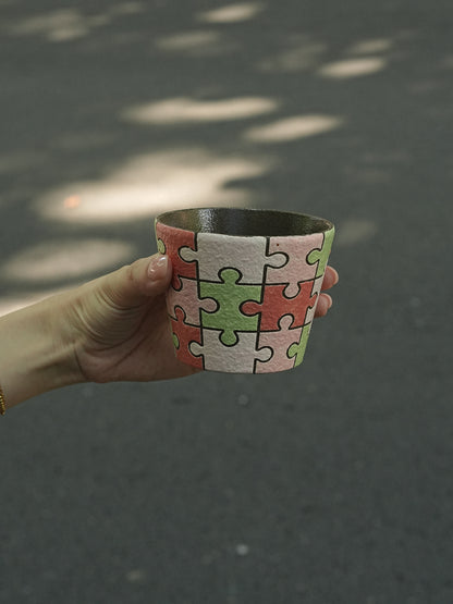 Close-up of a hand-painted puzzle ceramic cup with carved outlines in pink, green and ivory