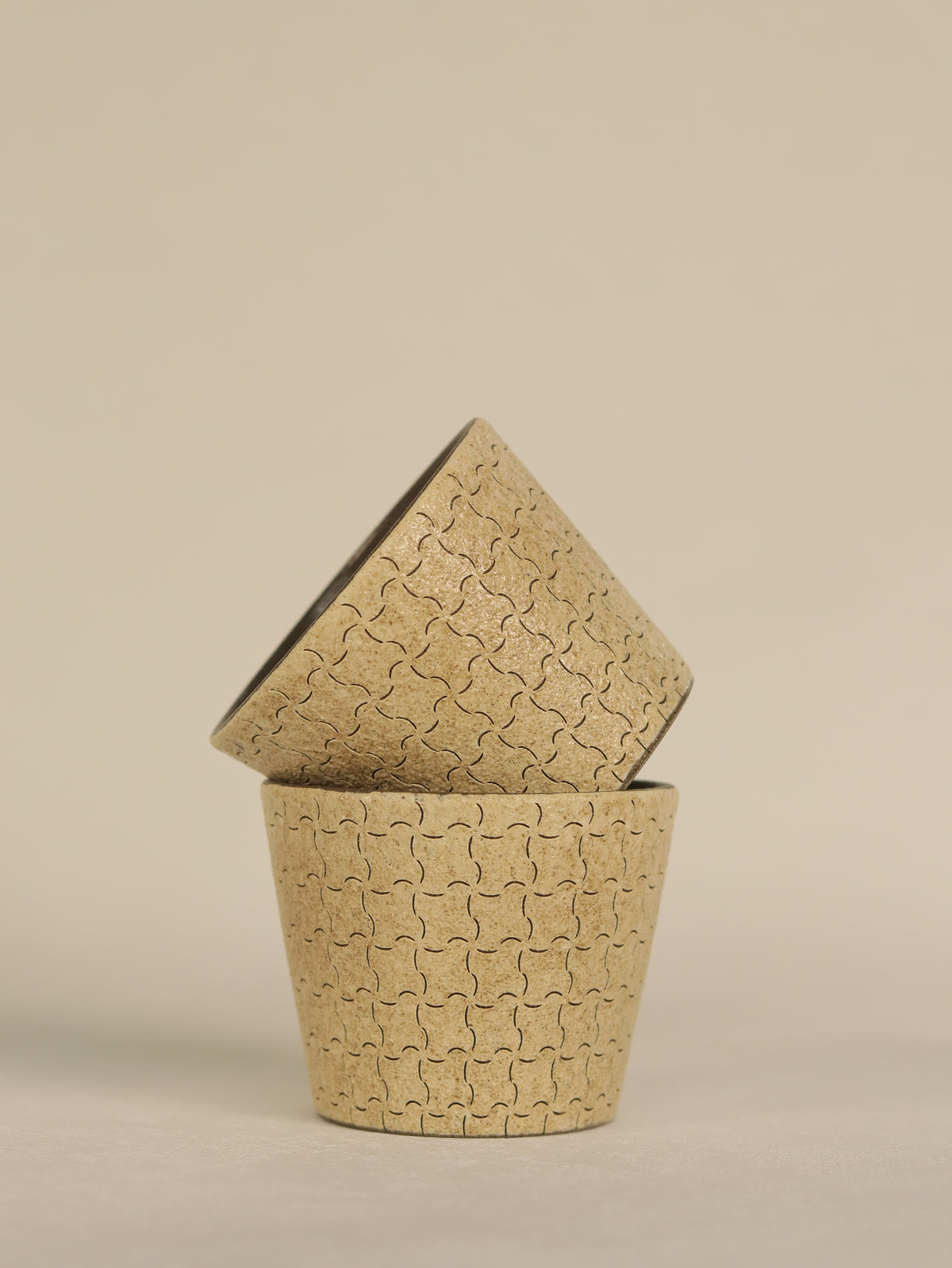 Two hand-carved geometric ceramic cups stacked together on a neutral background.