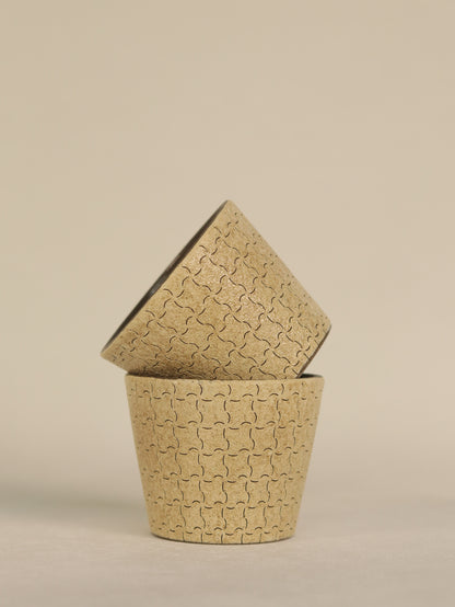 Two hand-carved geometric ceramic cups stacked together on a neutral background.