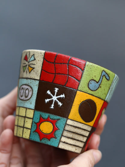 Colorful square tile with geometric patterns held by a hand against a gray background