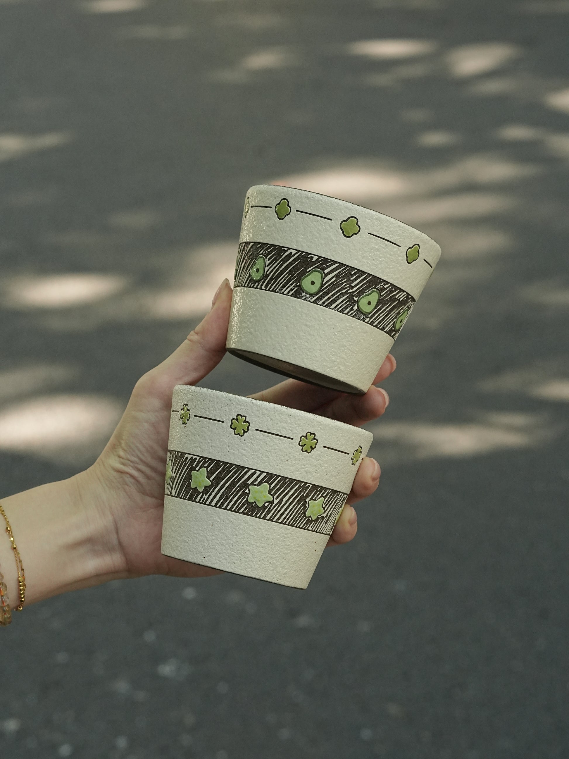 Two hand-painted green ceramic cups with avocado and star designs