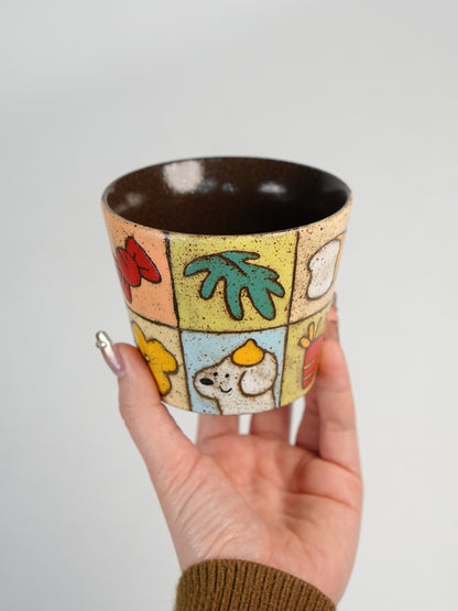 Hand holding a colourful ceramic cup with fruit, flower and leaf illustrations.