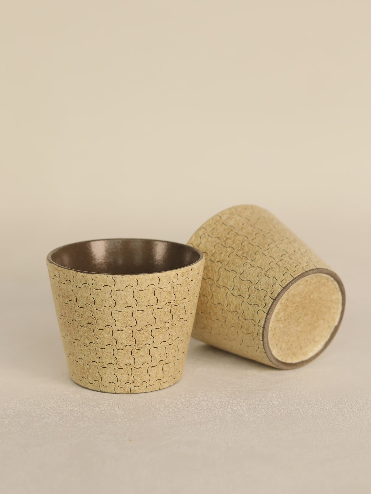 Two beige geometric ceramic cups displayed upright and on their side.