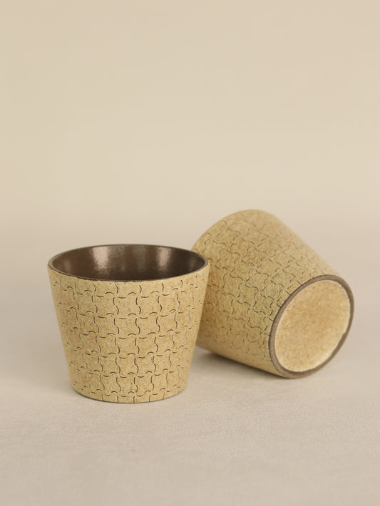 Two beige geometric ceramic cups displayed upright and on their side.