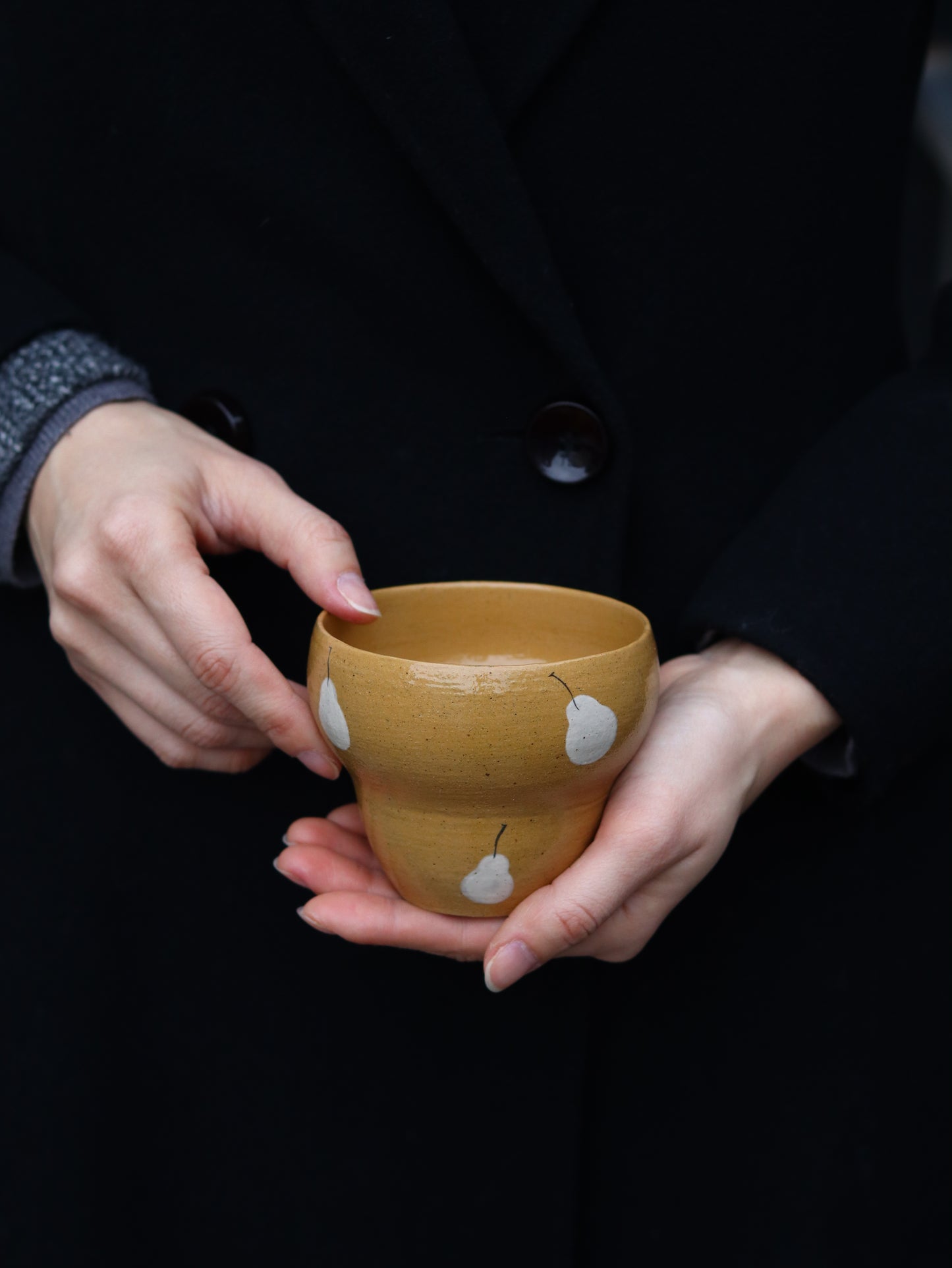 Person holding a small brown cup with white patterns against a dark background
