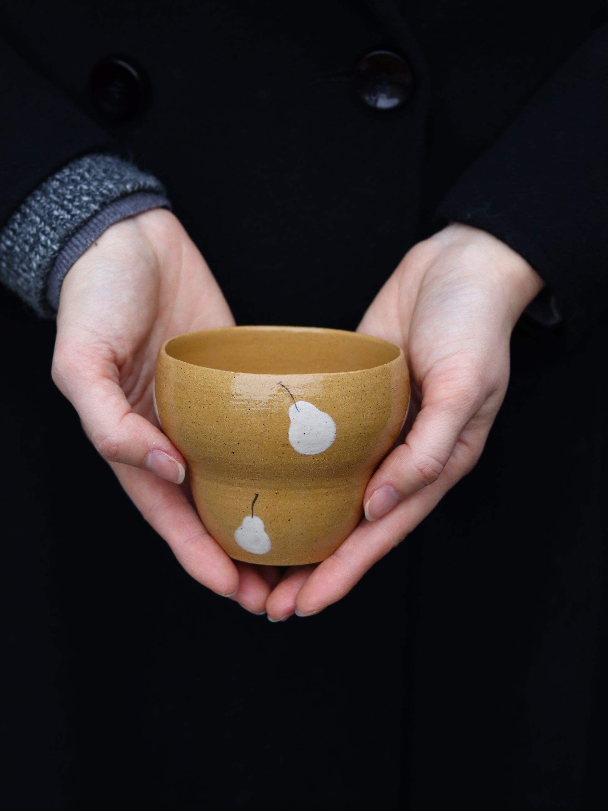 Person holding a small yellow ceramic bowl with white duck designs against a dark background