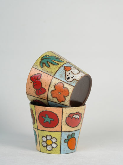 Two hand-painted patchwork ceramic cups stacked together on a neutral background.