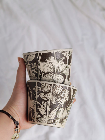 Hand holding two monochrome floral sgraffito ceramic cups