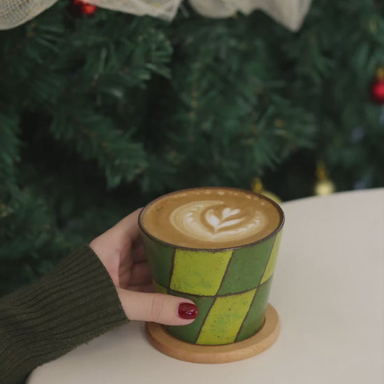 Small ceramic cup with green and brown geometric pattern on a beige surface