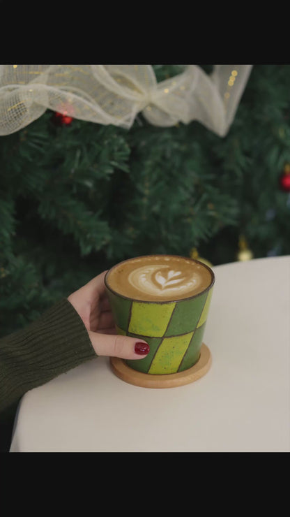 Small ceramic cup with green and brown geometric pattern on a beige surface