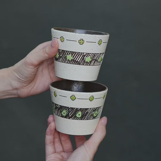Two hand-painted green ceramic cups with avocado and star designs